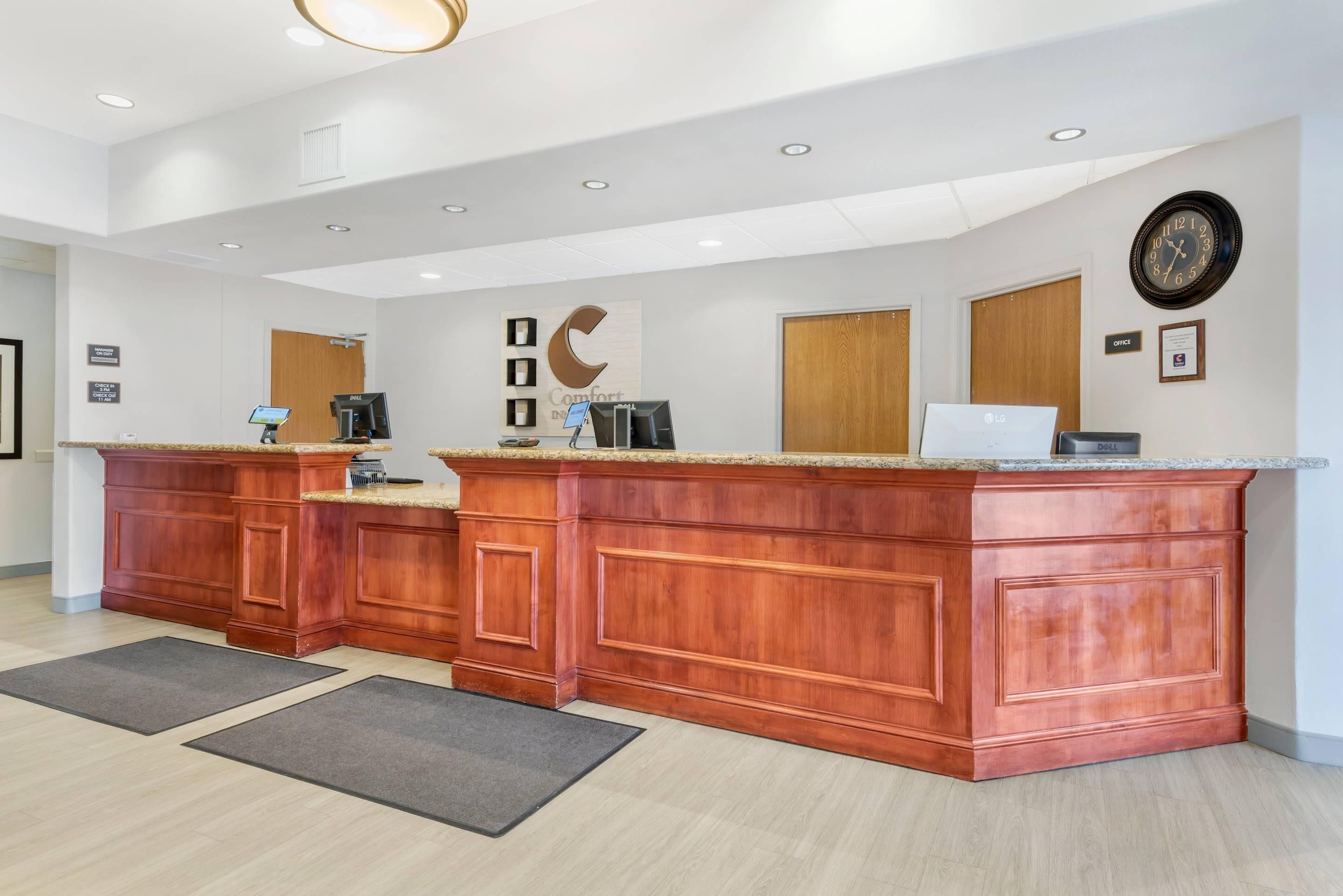 Un espace d’accueil avec un comptoir en bois, une horloge et un panneau indiquant les bureaux.