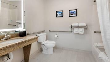Un baño moderno con lavamanos de granito, inodoro blanco, ducha con puerta de vidrio y dos cuadros enmarcados en la pared.