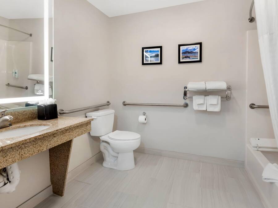 Un baño moderno con lavamanos de granito, inodoro blanco, ducha con puerta de vidrio y dos cuadros enmarcados en la pared.