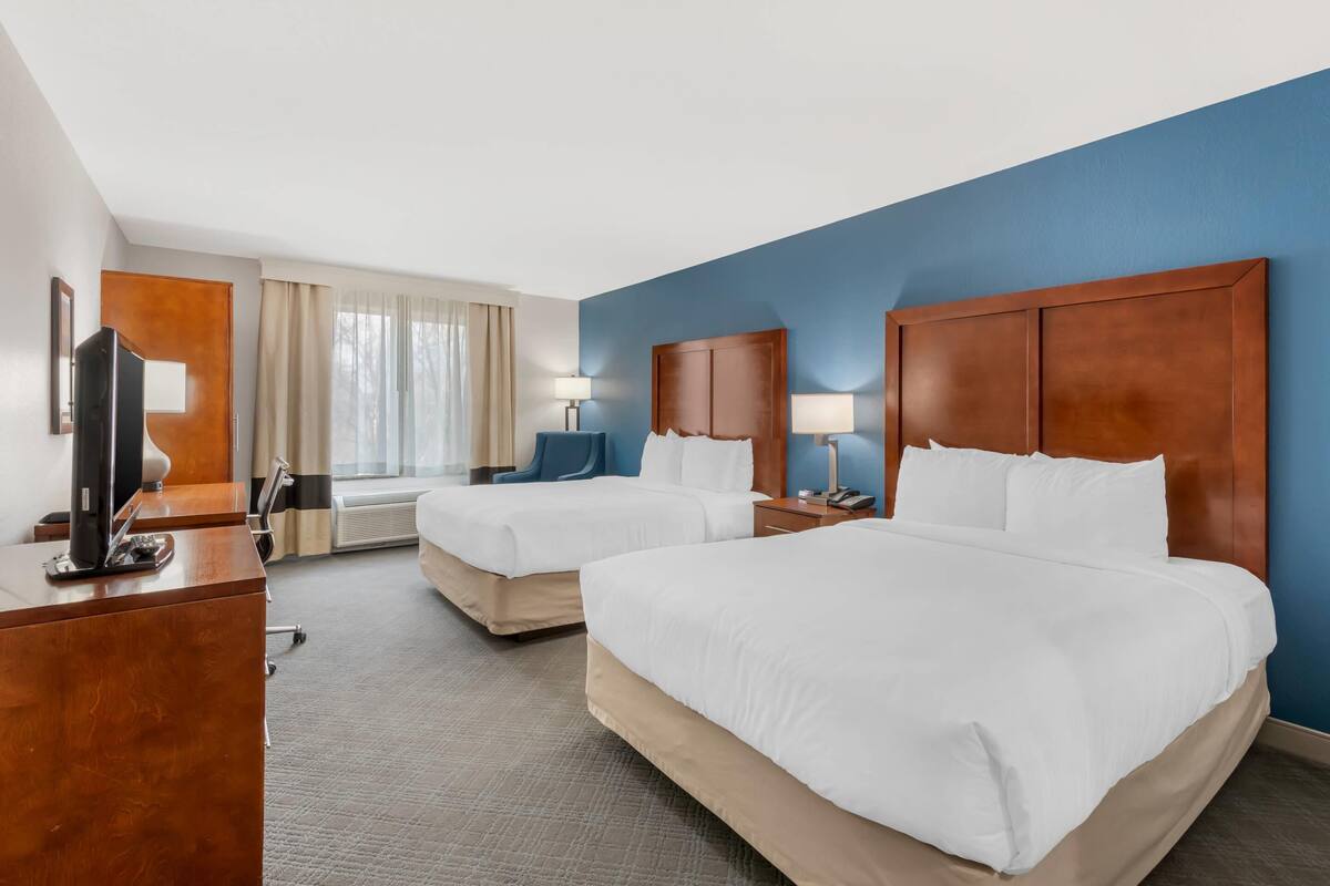A hotel room with two beds, a desk, a TV, and a window with curtains.