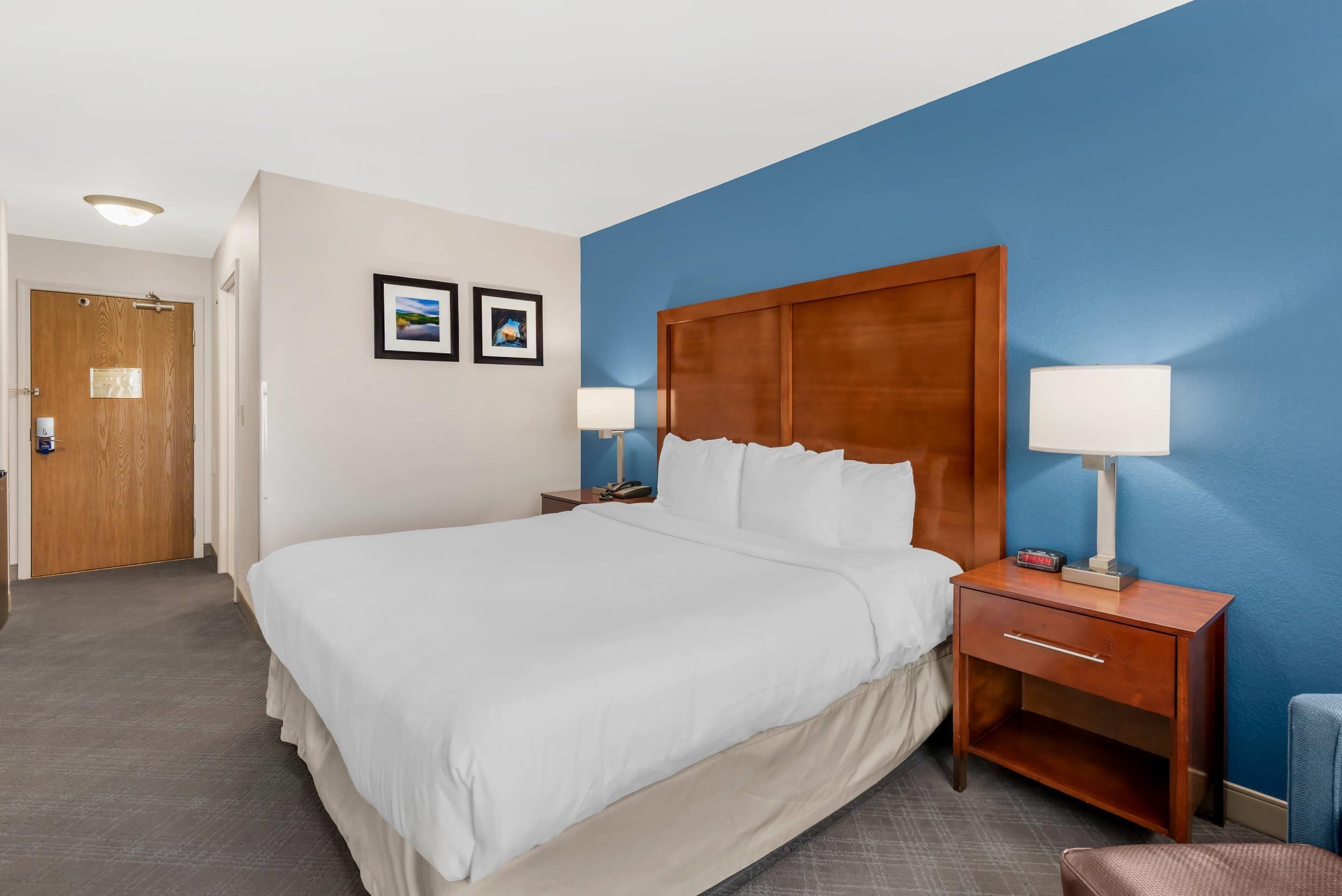 A hotel room with a large bed, two bedside tables with lamps, a wooden headboard, and a door with a light fixture.