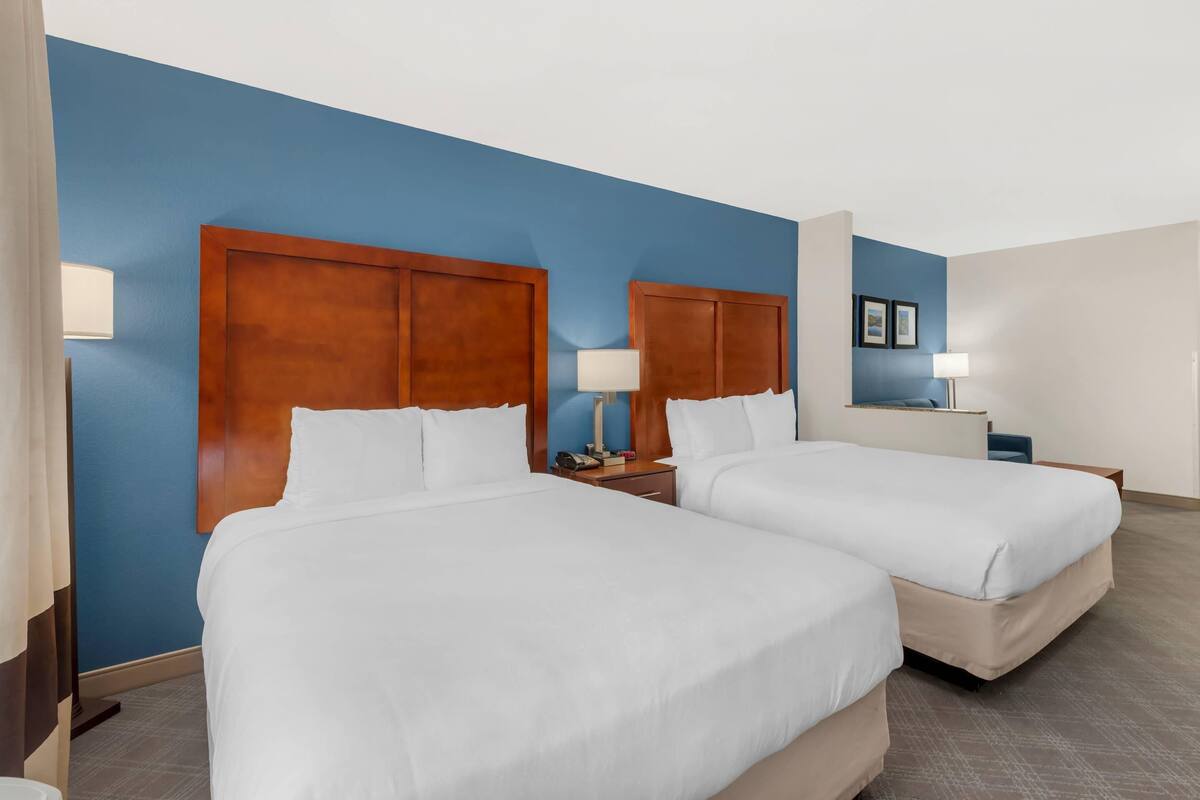 A hotel room with two beds, wooden headboards, and a blue accent wall.