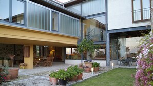 Una casa moderna con un patio, plantas en macetas y mobiliario exterior.
