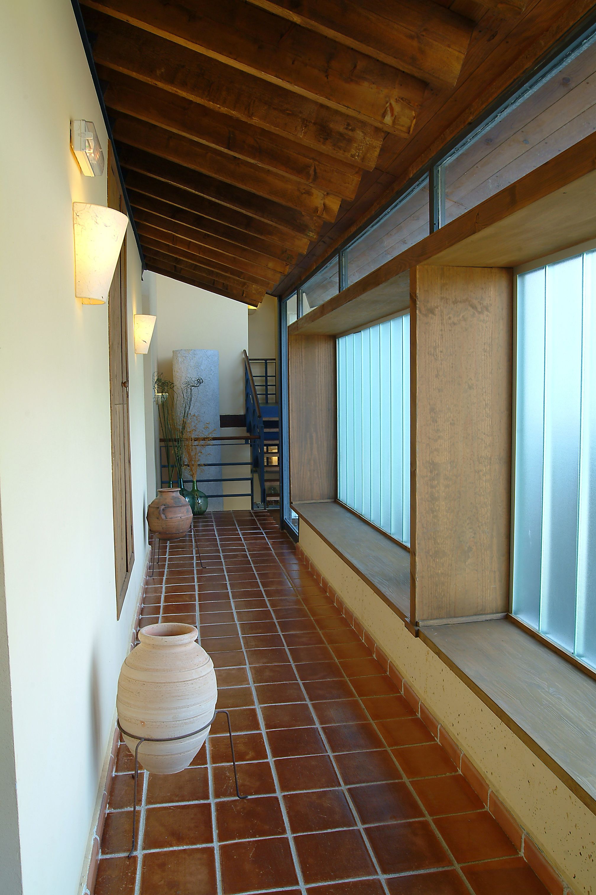 Un pasillo con suelo de baldosas, techo de madera y una ventana con persianas.