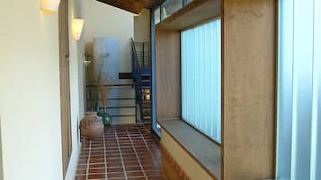 Un pasillo con suelo de baldosas, techo de madera y una ventana con persianas.