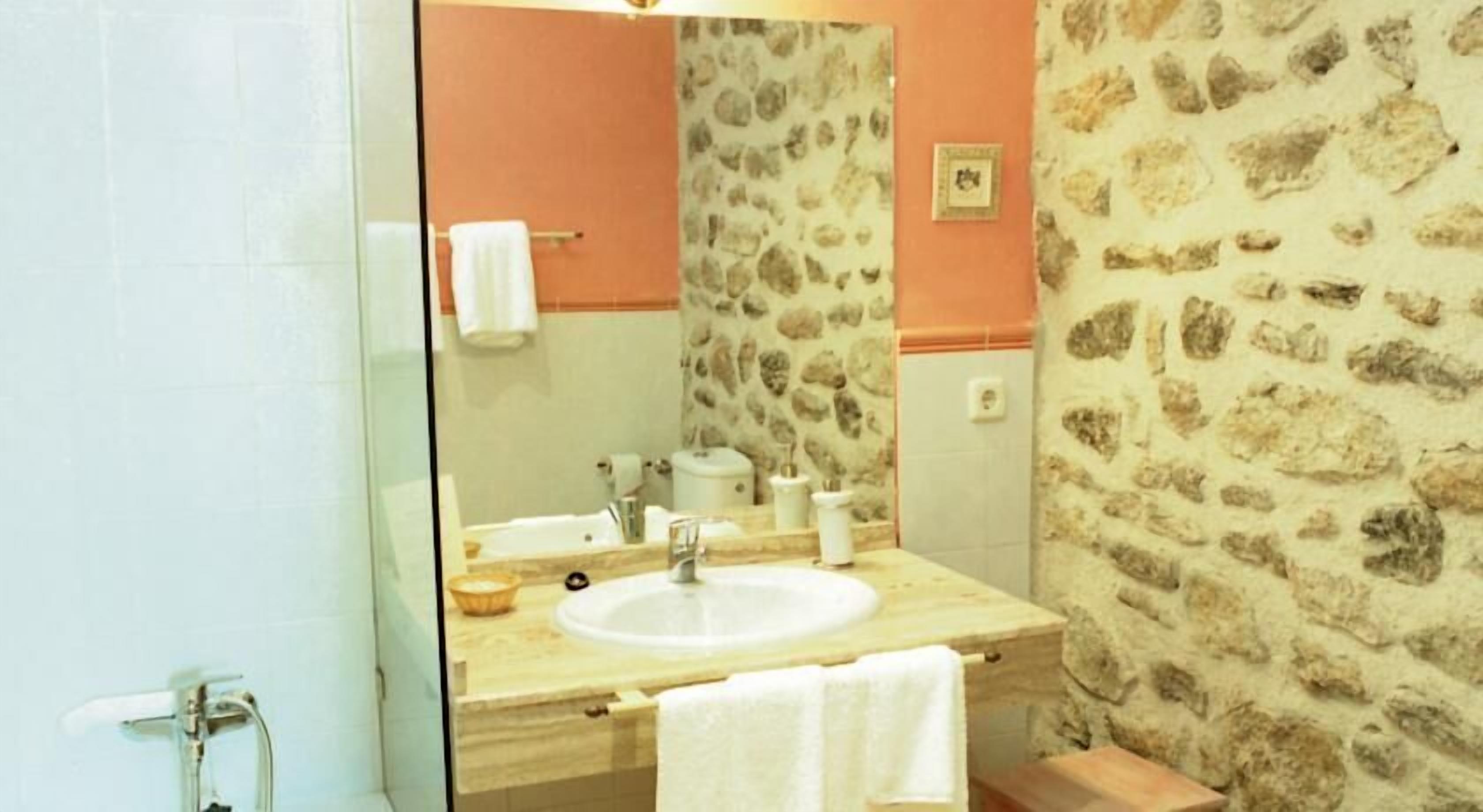 Un baño con pared de diseño de piedra, tocador de madera, lavamanos blanco y espejo.