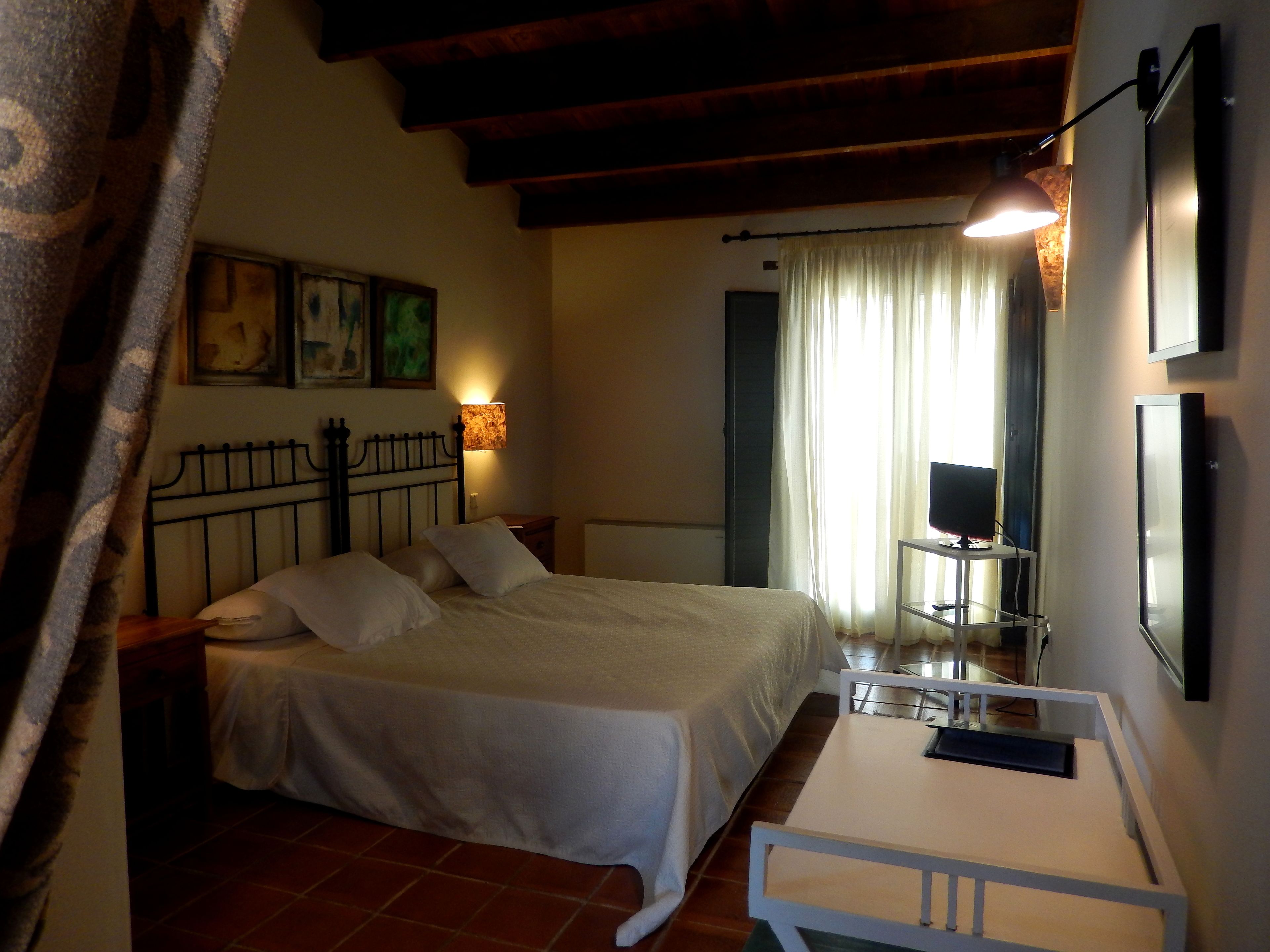 Un dormitorio con cama, mesita de noche, lámpara, televisor y cortinas.