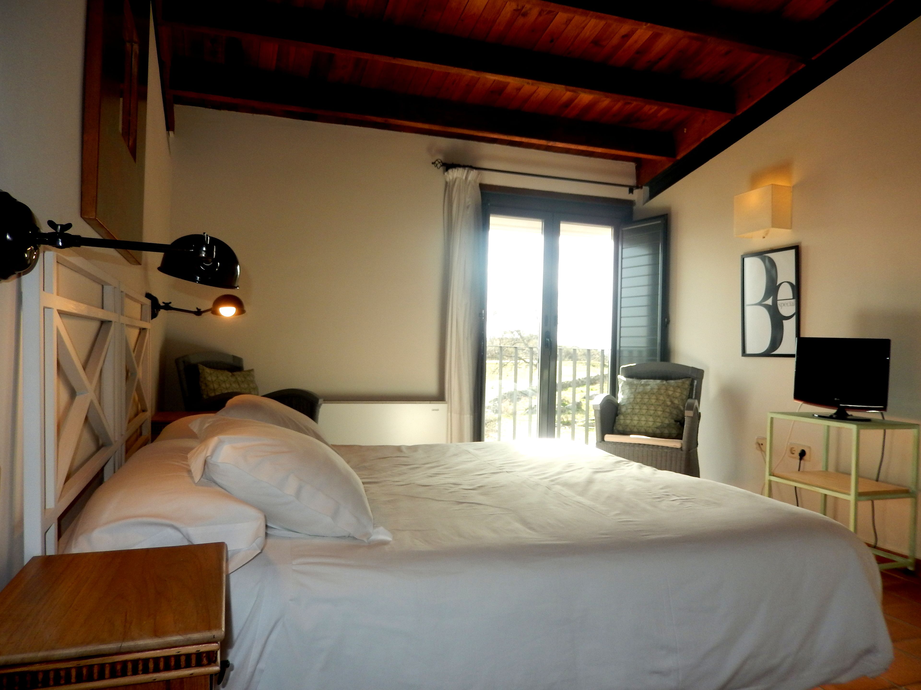 Un dormitorio con una cama grande, un escritorio, una silla, un televisor y un balcón con vistas.