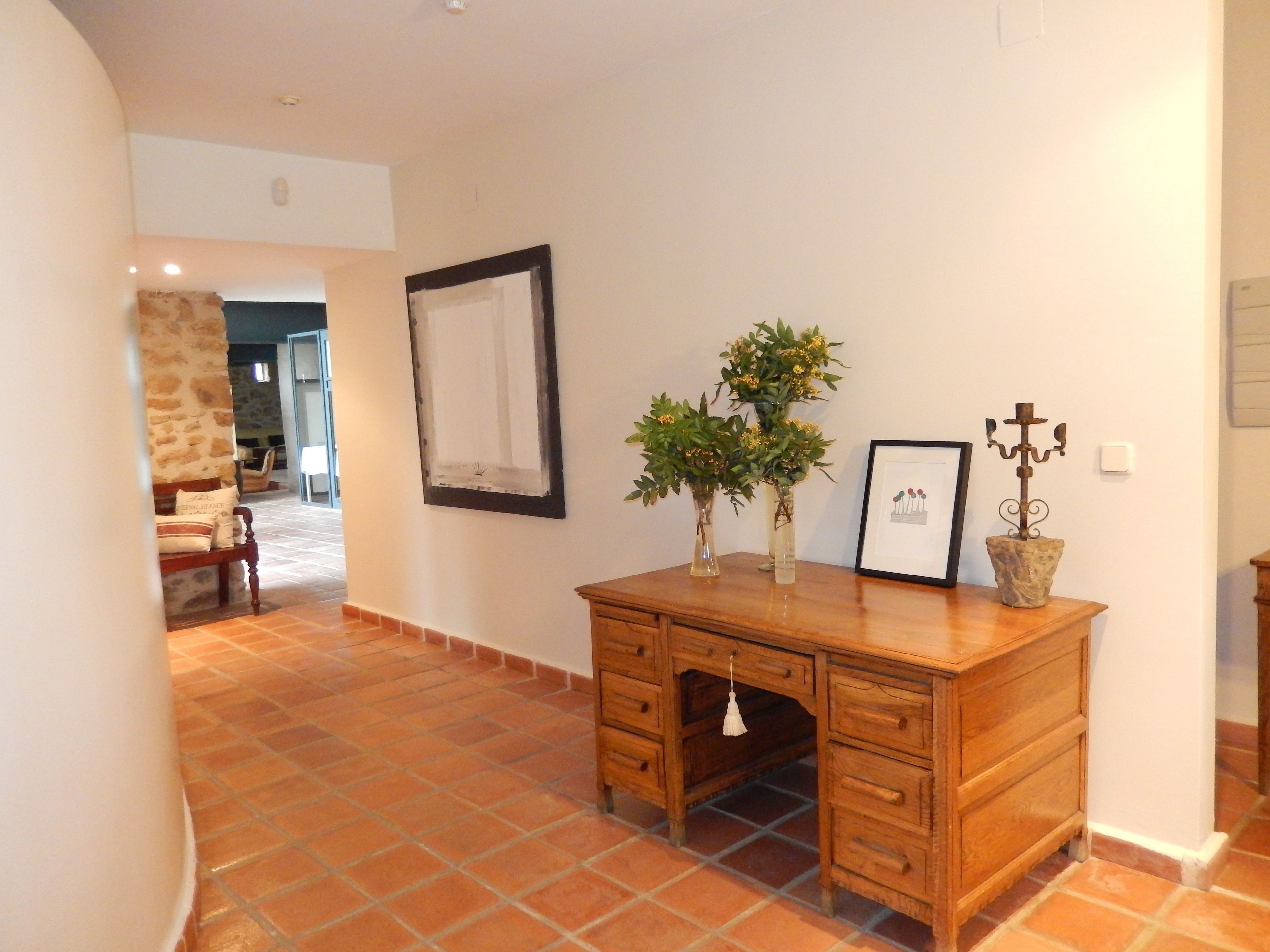 A spacious room with a wooden desk, two potted plants, a framed picture, and a candelabra.