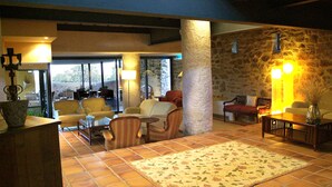 Amplia sala de estar con pared de piedra, un ventanal y vistas al exterior. Varias opciones de asientos, incluyendo un sofá, sillas y una mesa de centro.