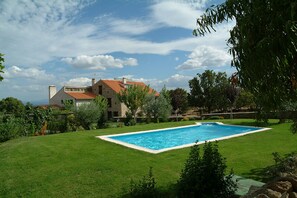 A swimming pool surrounded by a well-maintained lawn, with a stone house in the background.