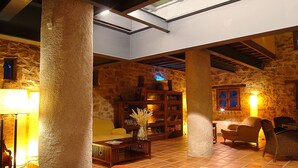Un interior acogedor con paredes de piedra, una estantería de madera y una zona de estar confortable con sofá y sillones.