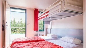 A bunk bed room with a red bedspread, white pillows, and a view of greenery outside. - Première Classe Valence Sud (Valence)