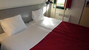 Una cama bien hecha con ropa de cama blanca y roja, una ventana con cortina roja y un calentador fijado a la pared.