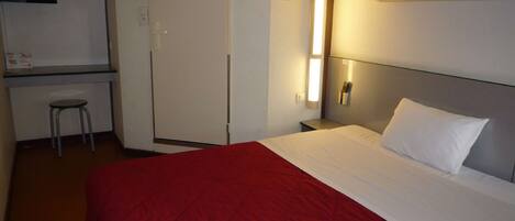A hotel room with a bunk bed, a desk with a chair, a bedside table, and a TV mounted on the wall.