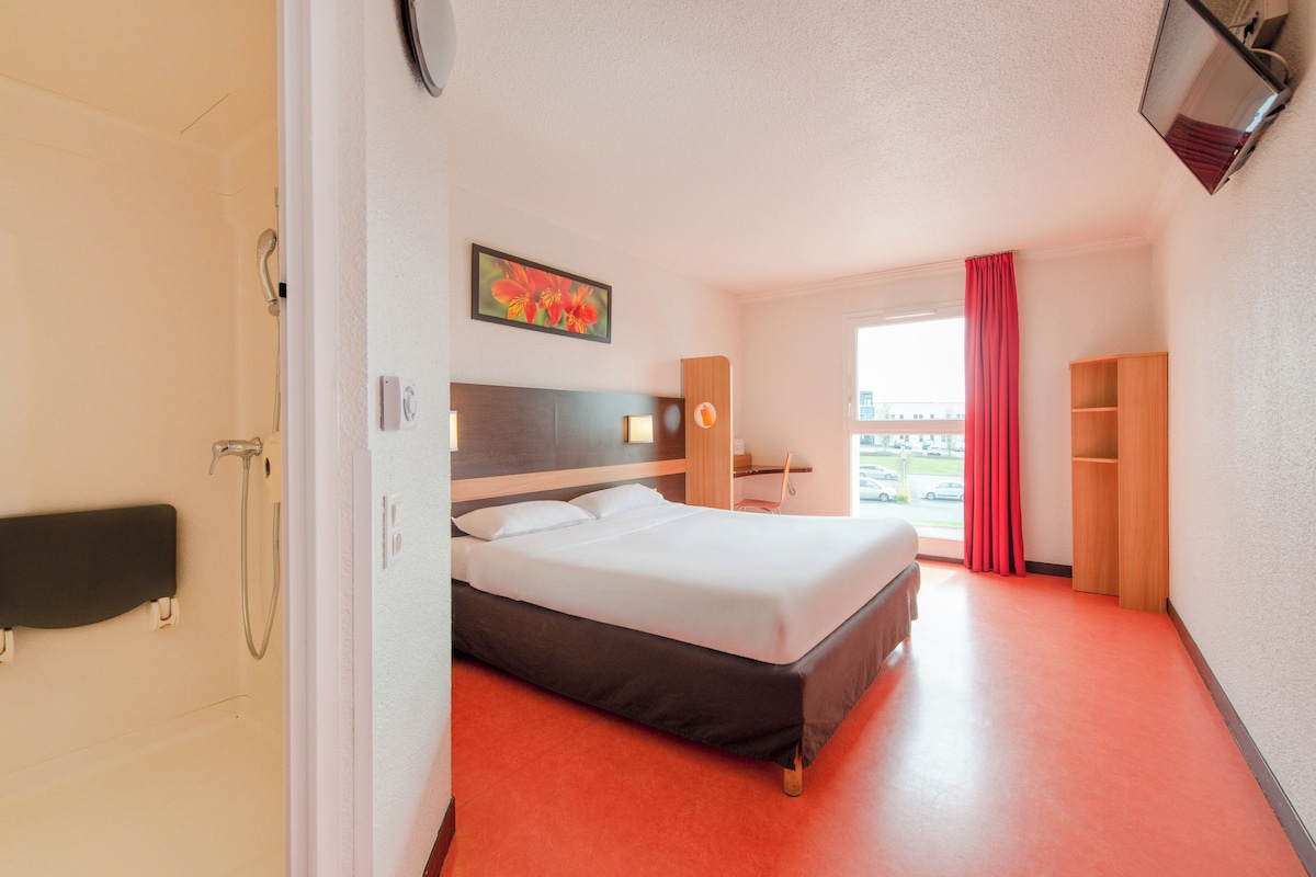 A hotel room with a bed, a desk, a chair, a TV, a wardrobe, and a window with curtains.