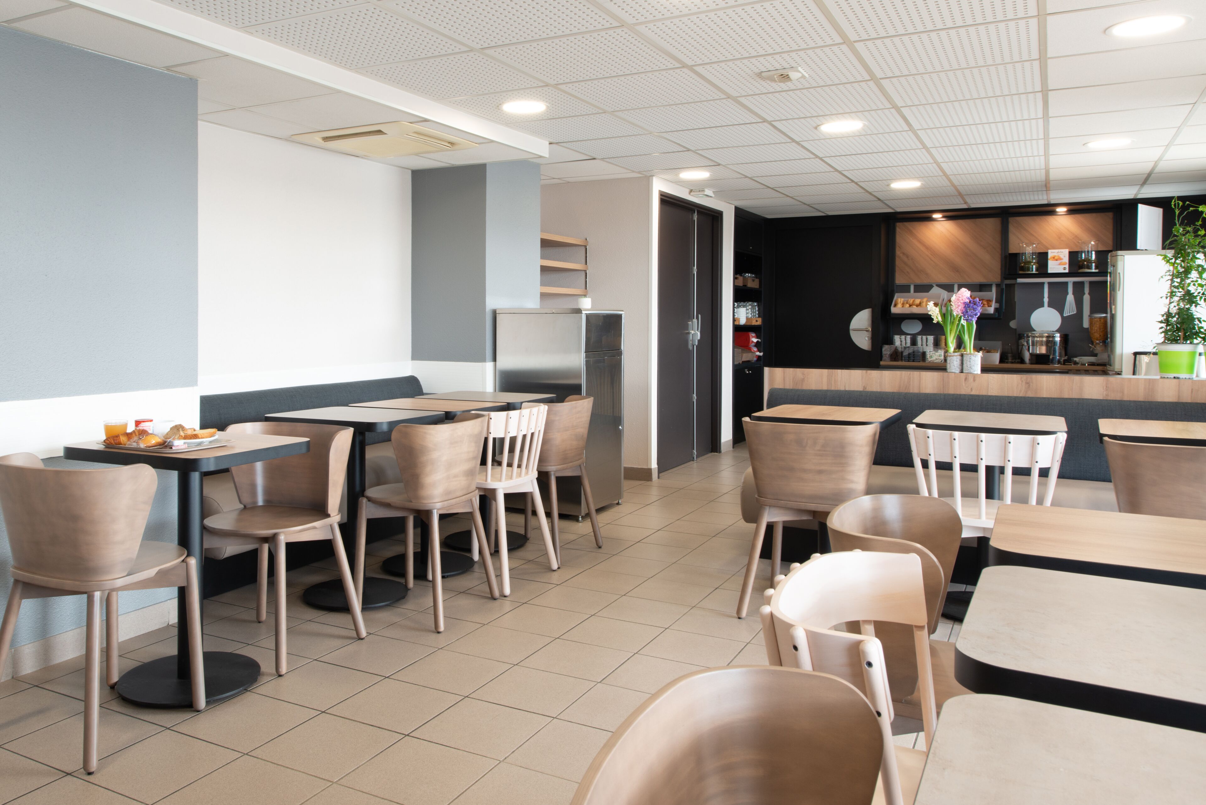A modern restaurant interior with multiple tables and chairs, a counter with a menu, and a refrigerator.
