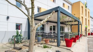 Een terras met tafels en stoelen, omgeven door potplanten en een boom.