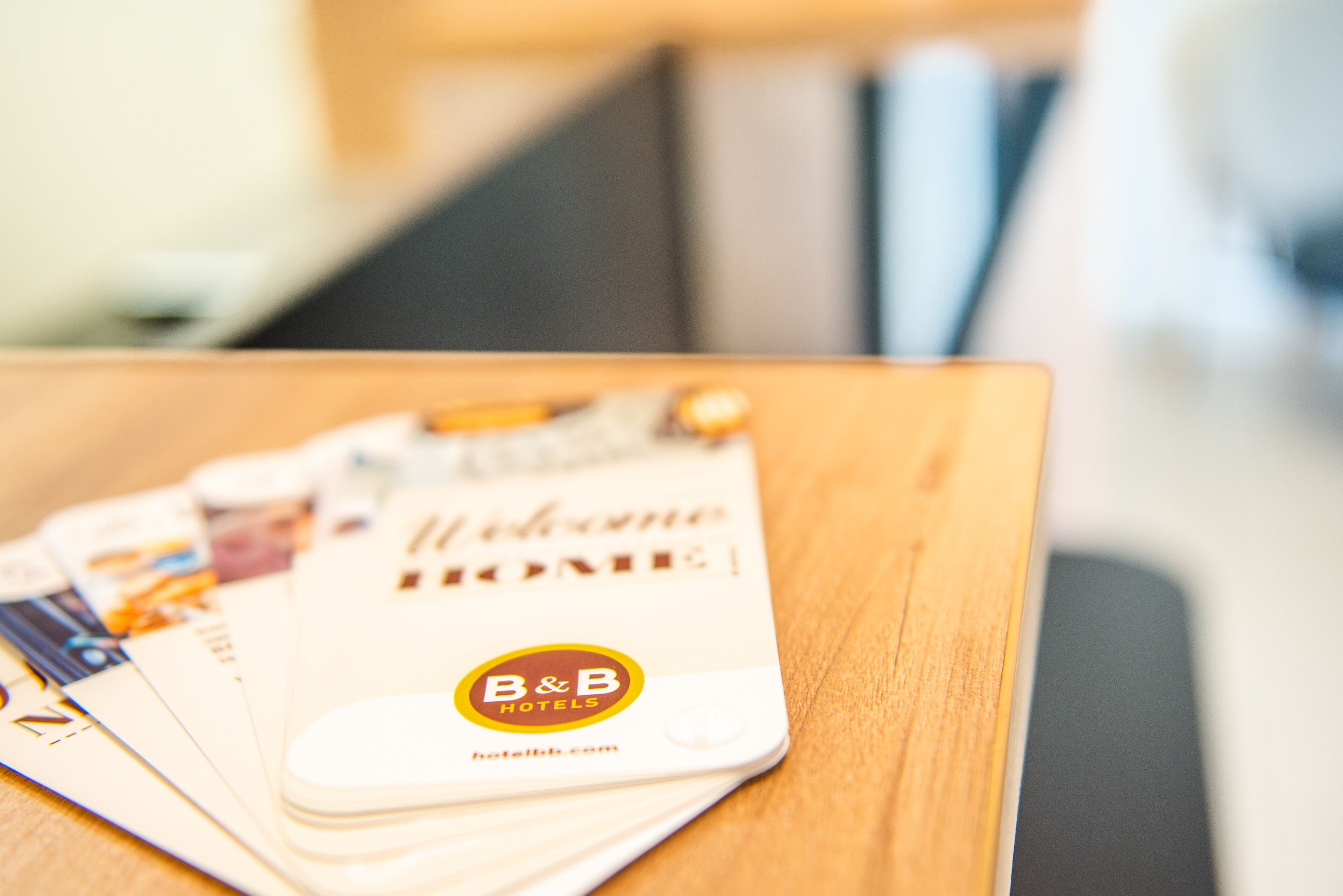 A brochure with the text "Welcome HOME" and the logo "B&B HOTELS" on a wooden surface.