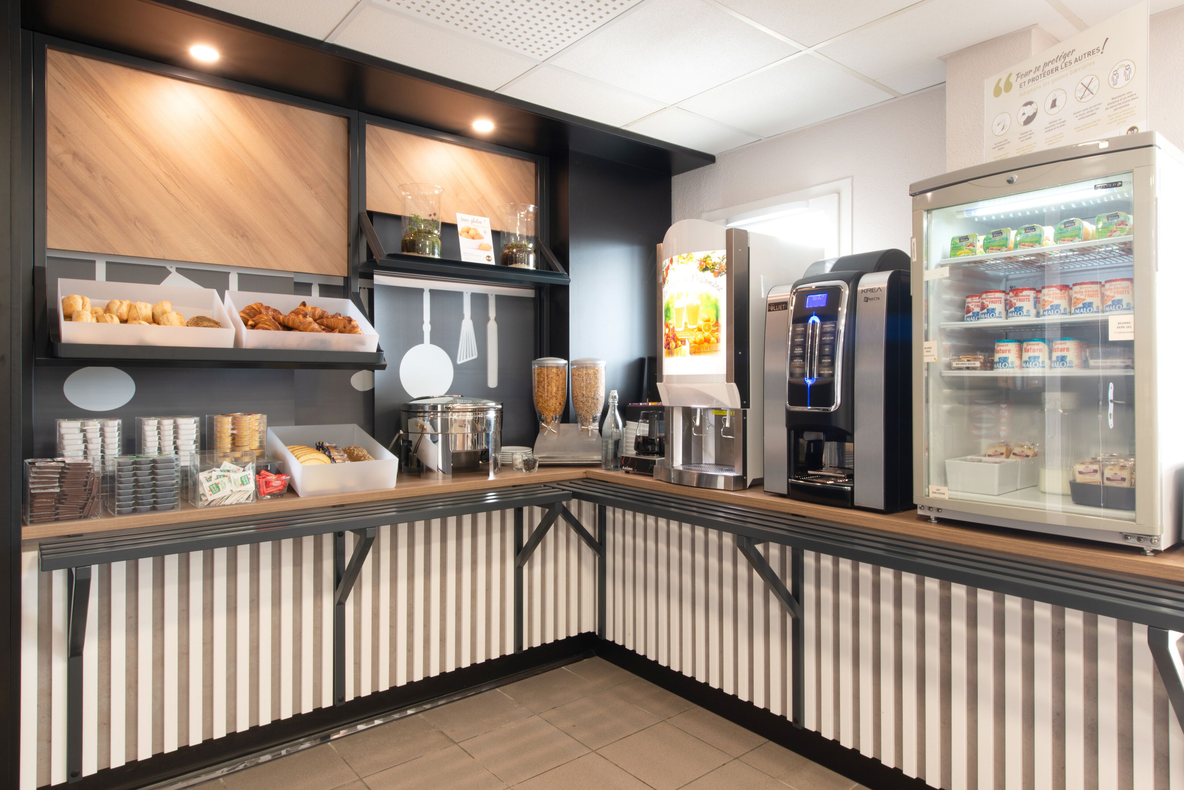 Un espace de petit-déjeuner en libre-service comprenant une machine à café, un présentoir réfrigéré et divers produits alimentaires.