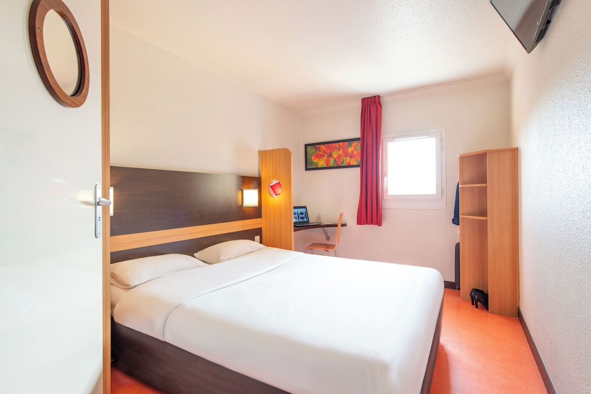 A hotel room with a bed, a desk, a chair, a TV, and a wardrobe.