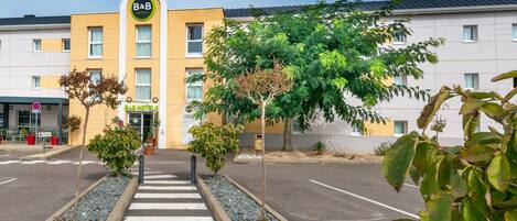 A B&B hotel with a yellow facade, a central entrance, and a parking lot with a zebra crossing.