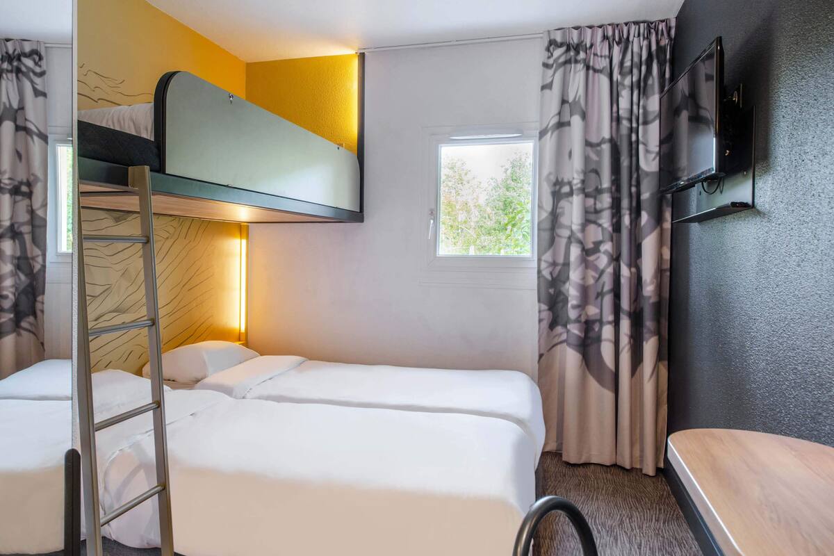 Una habitación con literas, un escritorio, un televisor y una ventana con cortinas.