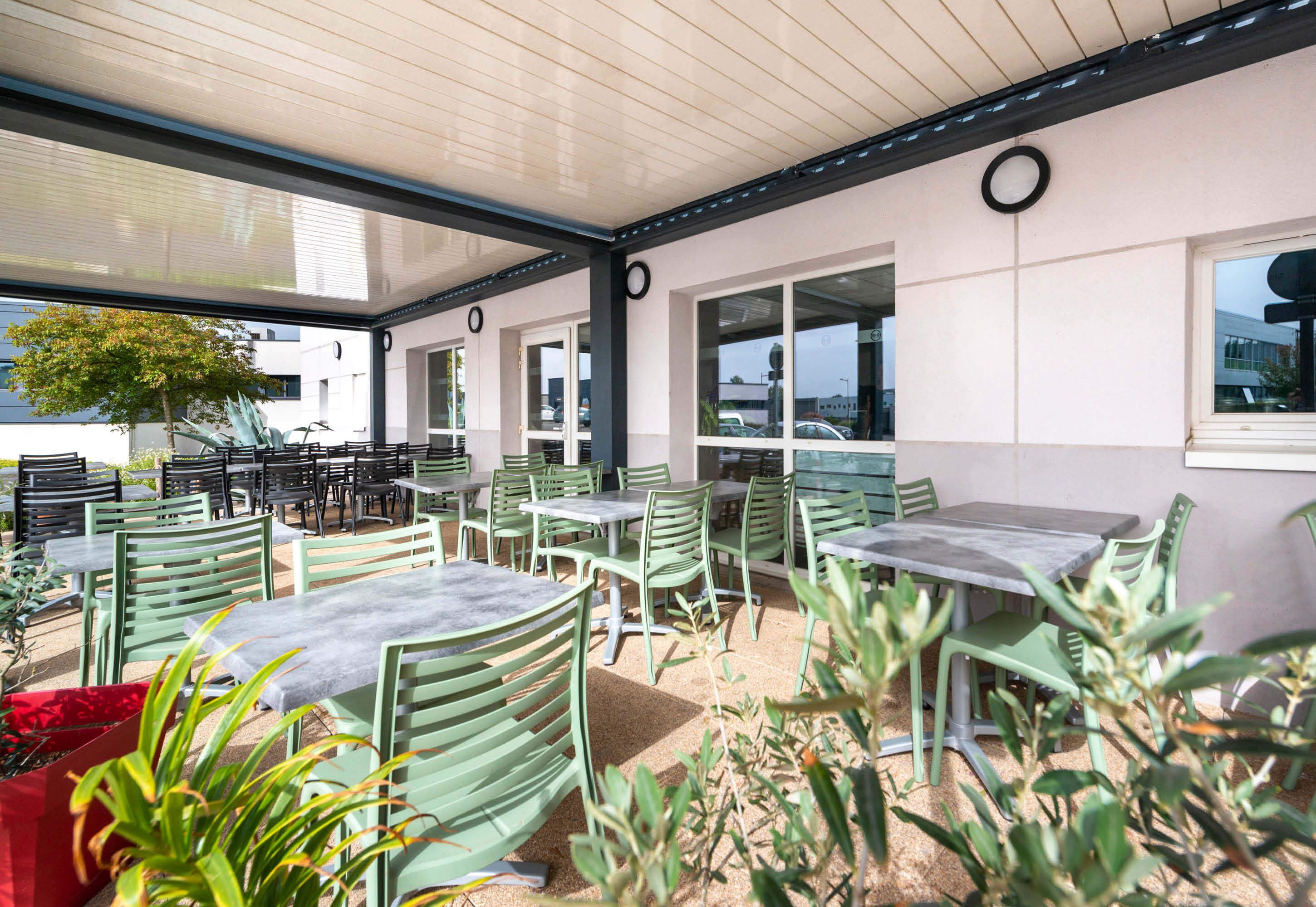An outdoor patio area with green metal tables and chairs, a covered seating area, and a view of the surrounding buildings.