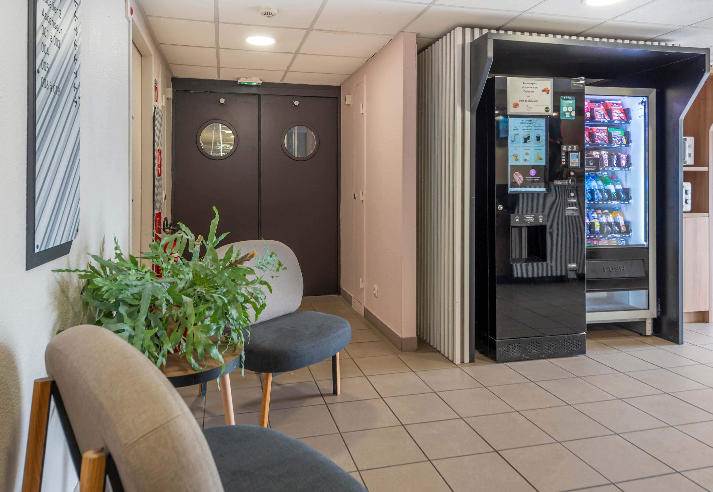 A hotel lobby with seating, a vending machine, and a door with a circular window.