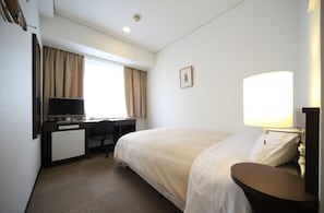 Una habitación de hotel con cama, escritorio, silla y un refrigerador pequeño.
