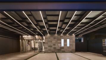 A modern hotel entrance with a flat roof, a stone facade, and a well-lit interior.