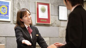 A reception area with a receptionist, framed certificates on the wall, and a stone-textured backdrop. - Hotel Park Side Hiroshima Peace Park (Hiroshima)