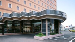Fachada curva de un hotel con amplias ventanas de vidrio y un cartel que dice 'OKAYAMA CITY'.