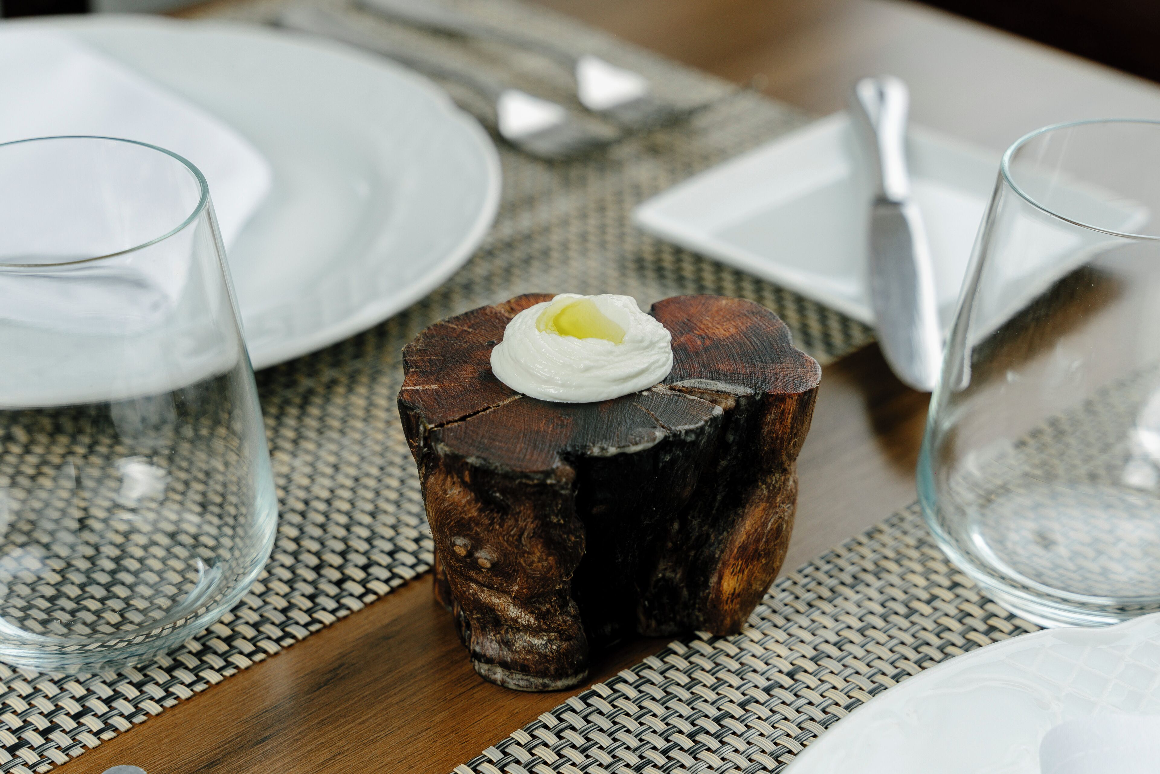 Una mesa de comedor con un original centro de mesa de madera, un plato blanco y una copa.