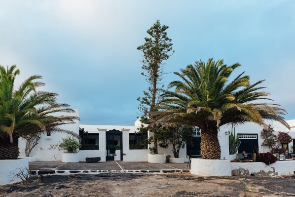 A white building with a black gate, palm trees, and a clear sky.