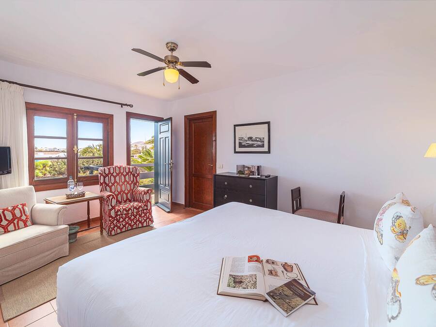 A hotel room with a bed, a chair, a desk, a television, a ceiling fan, and a window with a view.