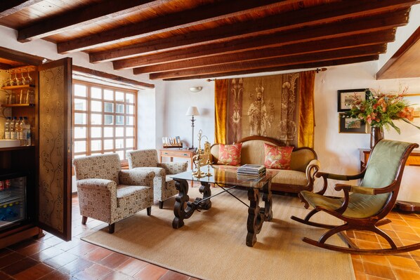 Un salón acogedor con muebles estampados, una mesa de centro de vidrio y un sillón mecedor de madera.