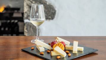 A cheese board with various cheeses, almonds, and grapes on a slate board, accompanied by a wine glass.