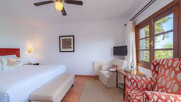 A hotel room with a bed, a desk, a chair, a television, and a window with a view of trees.