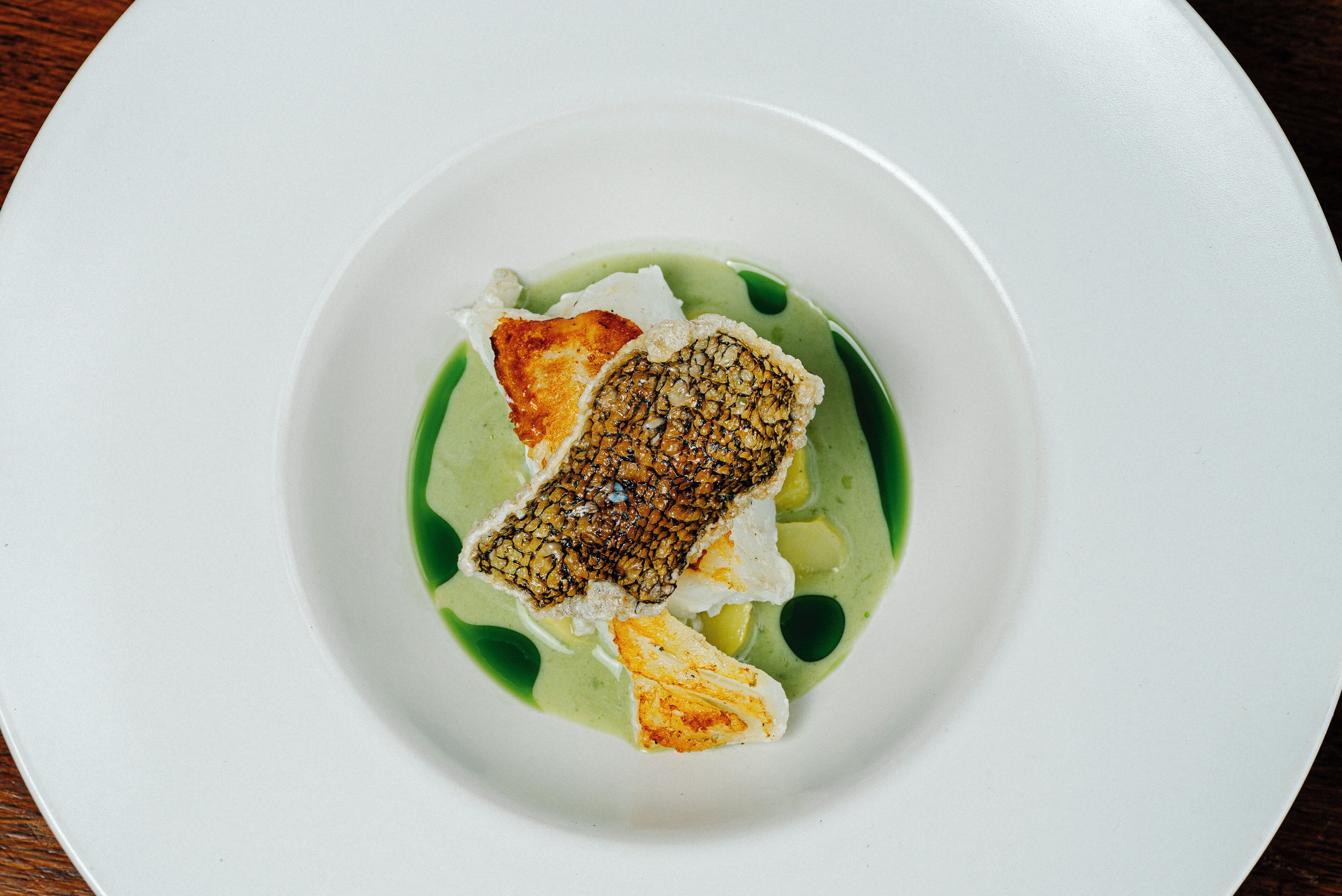 A white plate with a piece of fish and a green sauce.
