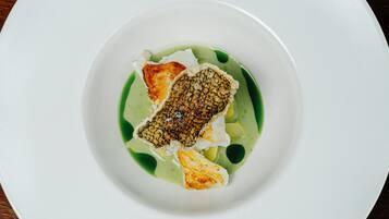 A white plate with a piece of fish and a green sauce.