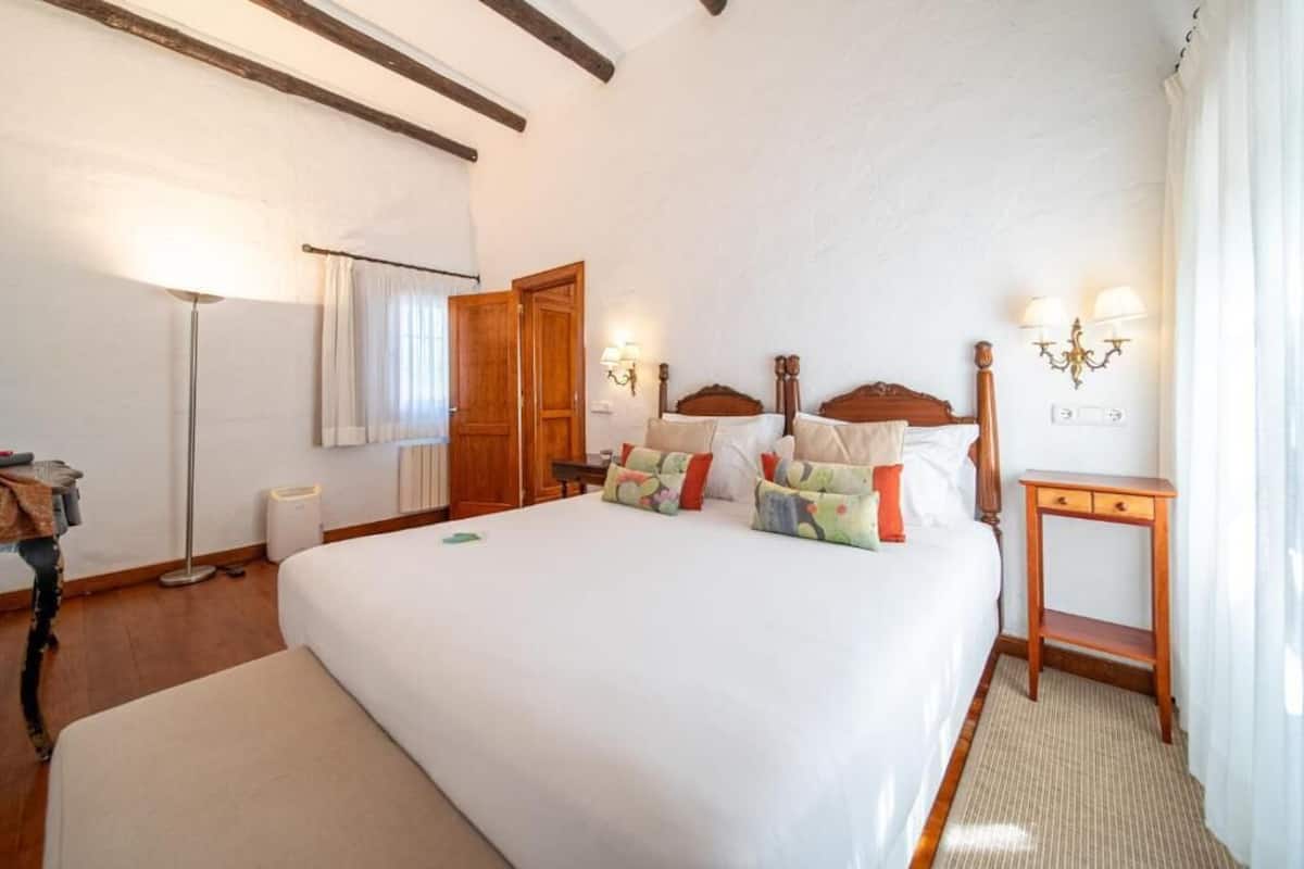 Una habitación de hotel con una cama grande, lámparas de noche, una mesita de noche de madera y una lámpara de pie.