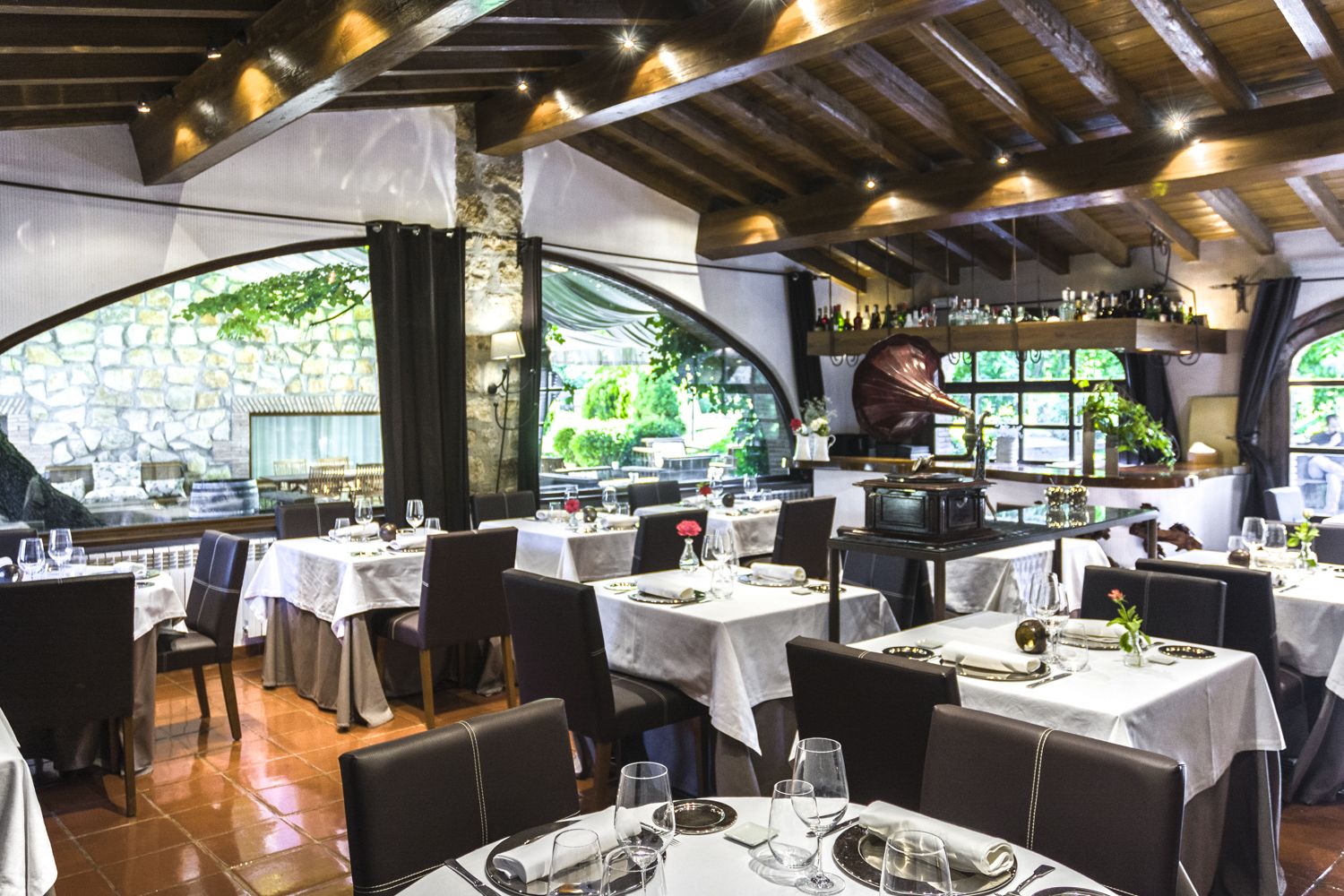Un restaurante con mesas dispuestas para comer, una zona de bar y vistas al exterior con vegetación.