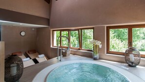 A spa room with a hot tub, wooden ceiling beams, large windows with a view of greenery, and a clock on the wall. - Hotel-SPA El Molino de Alcuneza (Siguenza)