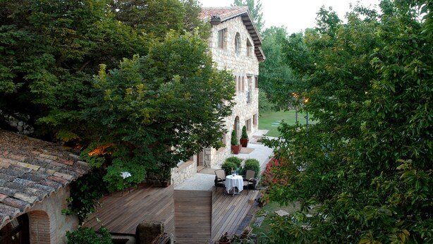 A stone building with a wooden deck and outdoor seating area surrounded by lush greenery. - Hotel-SPA El Molino de Alcuneza (Siguenza)