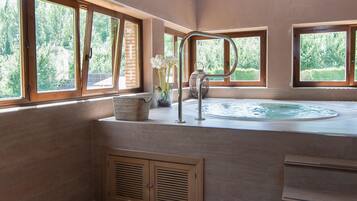 Relax in a serene space with a large hot tub and views of lush greenery.