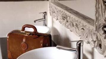 Un baño con un lavabo blanco, un bolso de cuero marrón y un espejo con detalles ornamentales.