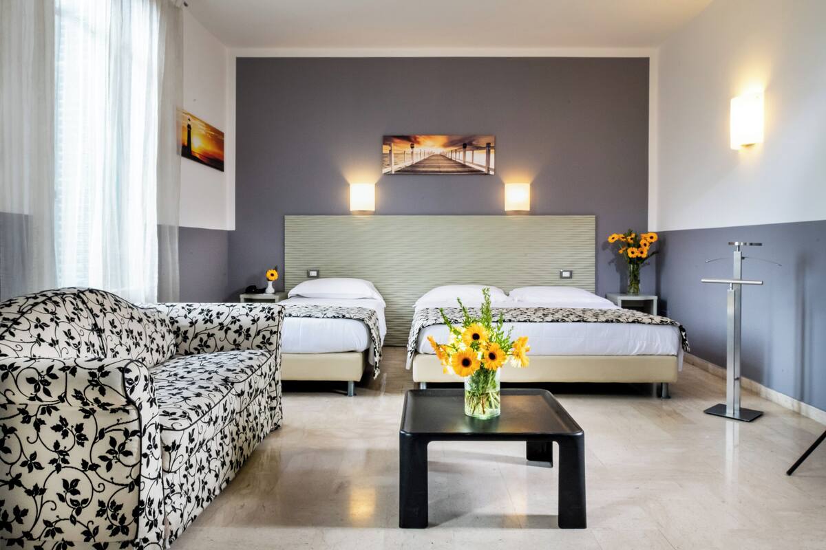 Une chambre d’hôtel avec deux lits, un canapé, une table basse ornée de fleurs et un tableau au mur.