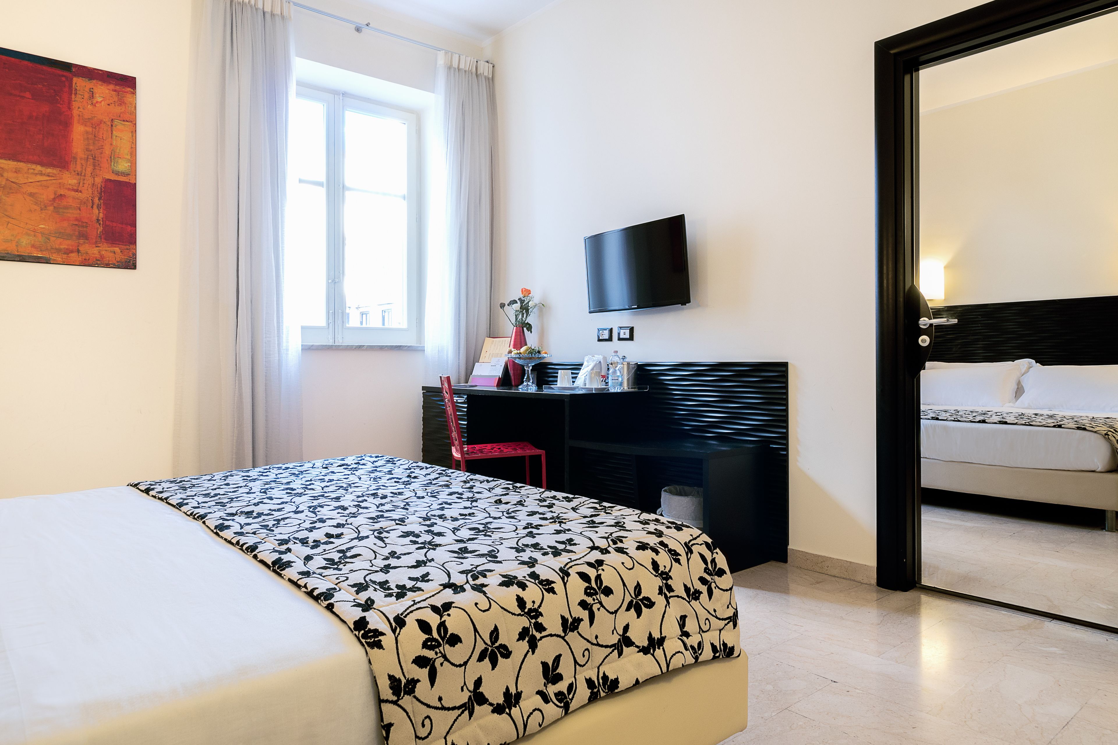 A hotel room with a bed, a desk, a TV, and a view of the outside.