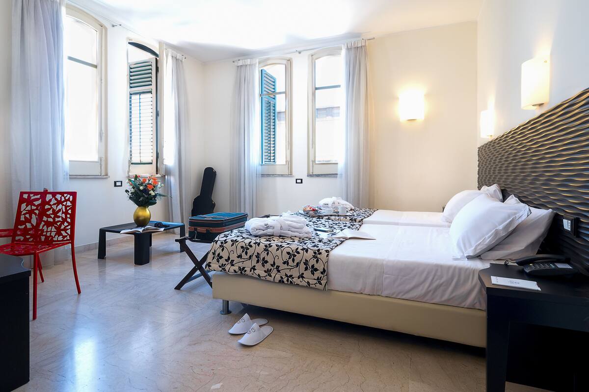 Une chambre d’hôtel avec un lit, un bureau, une chaise et une fenêtre avec des rideaux.